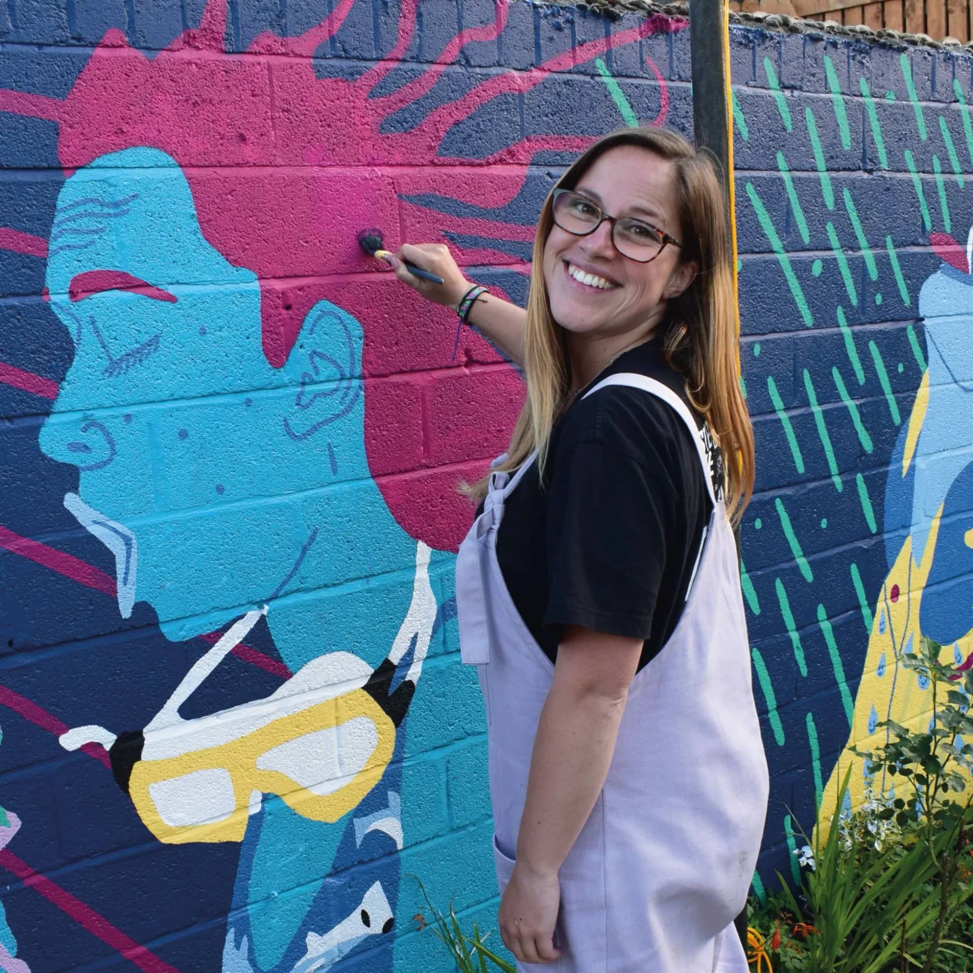 Hazel Oakes smiling as she paints a large blue and pink mural face