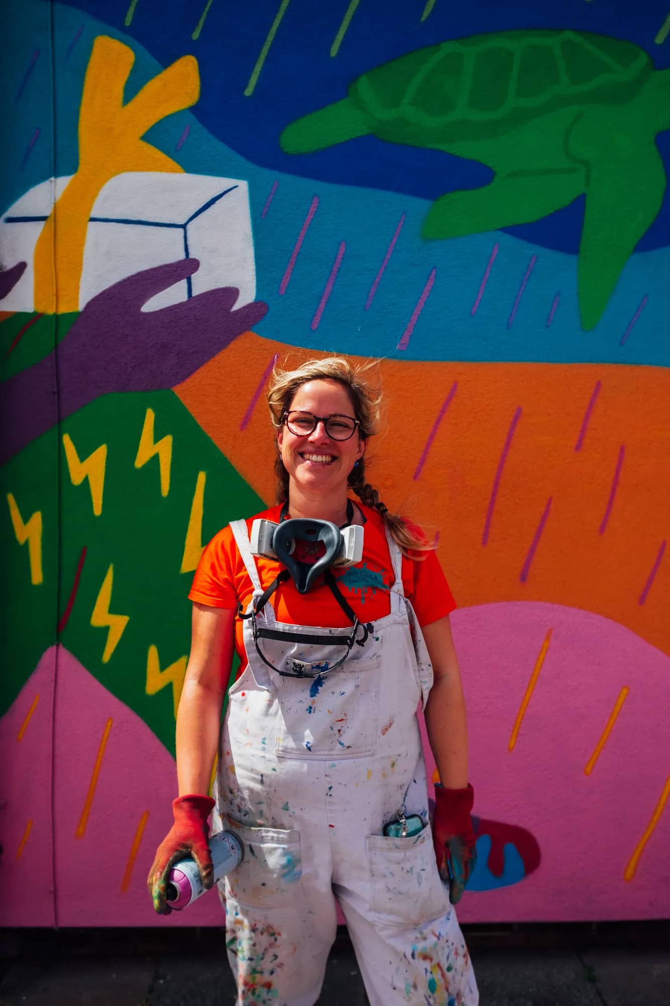 Hazel Oakes holding a spray can in front of the Stories of Home mural