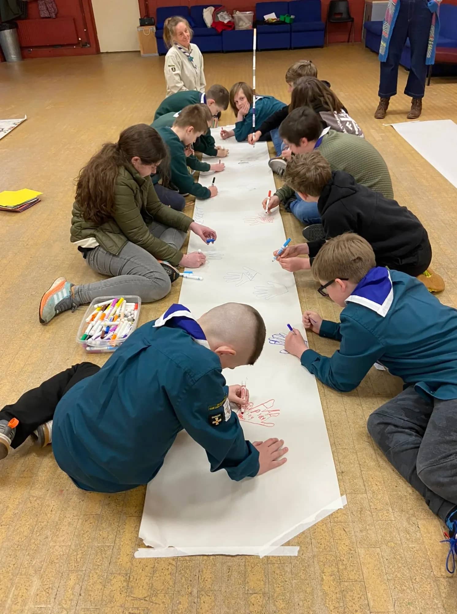Children drawing together on a long roll of paper laid across a hall floor