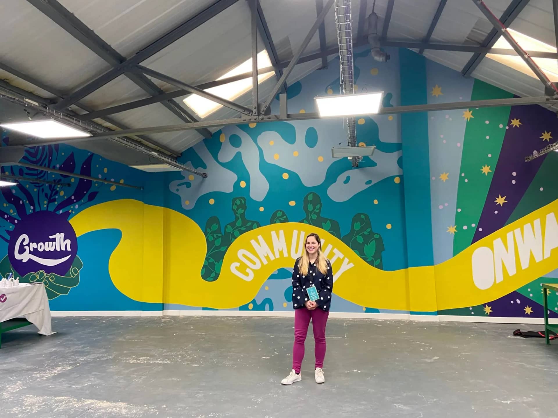 Hazel standing in front of the Growth mural in a large hall