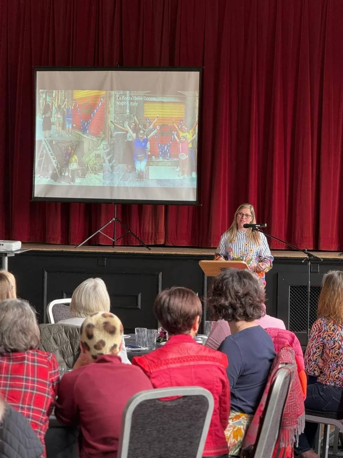 Hazel on stage at a lectern with her slides behind her